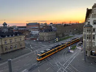 Blick von oben auf das Gleisviereck Schlachthof, Durlacher Allee und Tullastraße von schräg oben. Die untergehende Abendsonne taucht das Bild in eine dunkel-orangefarbene Lichtstimmung. 