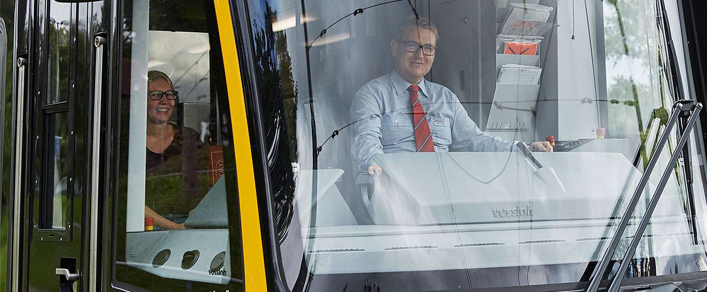 Ein Bahnfahrer sitzt lächelnd in der Fahrerkabine.