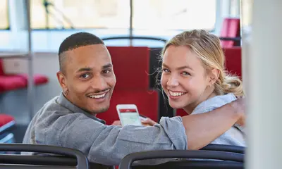 Ein junges Paar sitzt in einer Trambahn. Die Frau hält ein Smartphone in der Hand.