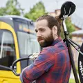 Ein junger Mann in karriertem Hemd trägt ein Fahrrad über der Schulter. Im Hintergrund sieht man eine Bahn der KVV.