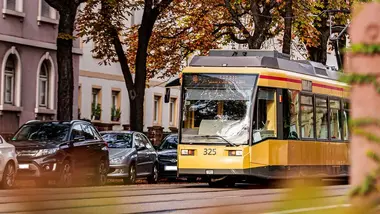 Eine Bahn der Tramlinie 4 bei einer Fahrt durch die Karlsruher Weststadt. Neben der Bahnstrecke sind parkende Autos und Bäume zu sehen.