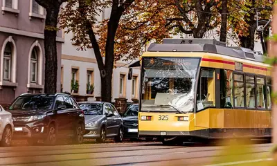 Eine Bahn der Tramlinie 4 bei einer Fahrt durch die Karlsruher Weststadt. Neben der Bahnstrecke sind parkende Autos und Bäume zu sehen.