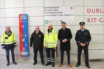 Fünf Verrter von VBK, Polizei und Rettungsdiensten stehen vor einer Notrufsäule an einem Bahnsteig des Karlsruher Stadtbahntunnels.