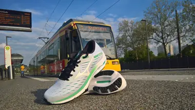 Ein Paar Laufschuhe liegt auf dem Bahnsteig einer Haltestelle. Im Hintergrund hält eine Trambahn.