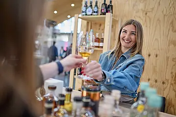 An einem Messestand der "EUROVINO reicht eine Frau einem Messe-Besucher ein Weinglas. 
