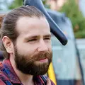 Ein junger Mann trägt ein Fahrrad über der Schulter. Hinter ihm ist eine Bahn der KVV.