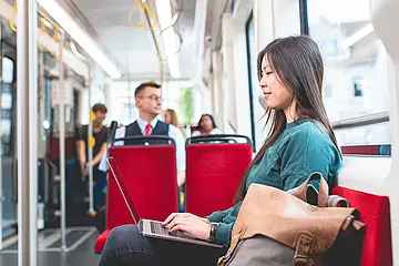 Junge Frau sitzt in der Bahn an ihrem Laptop.