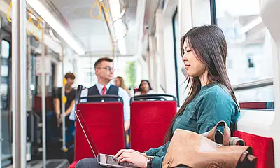 Junge Frau sitzt in der Bahn an ihrem Laptop.
