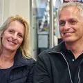 Eine ältere Frau und ein Mann sitzen in einer Bahn und reden miteinander.