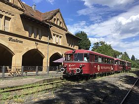 Der historische rote Schienenbus "Kloster Flitzer" hält an einem Bahnsteig vor dem Bahnhofsgebäude in Maulbronn