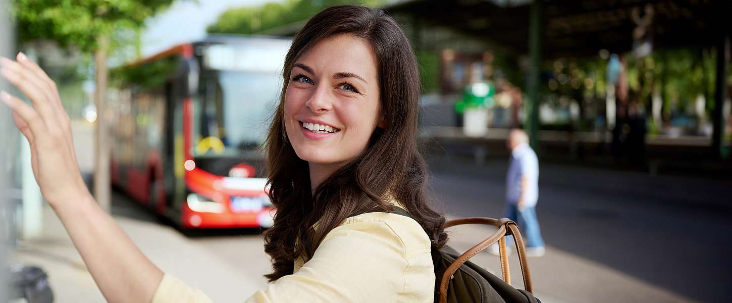 Eine junge Frau steht lächelnd an einem Fahrkartenautomat.