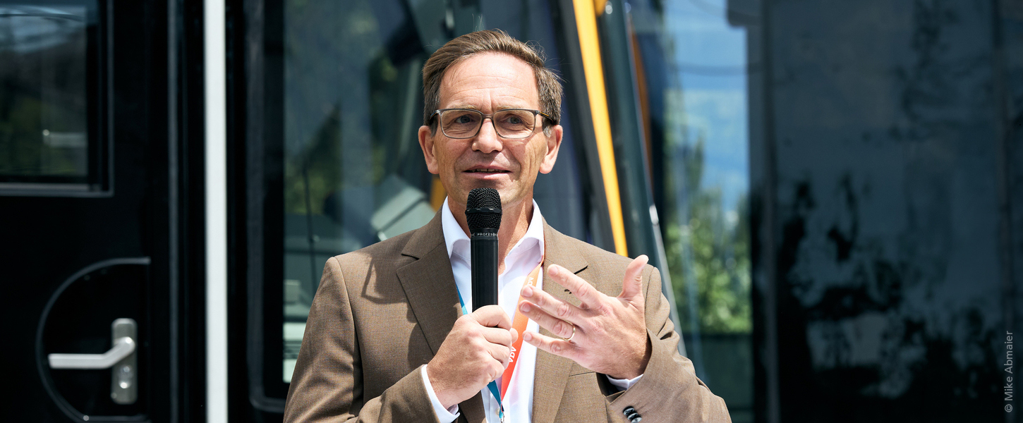 Der technische Geschäftsführer Christian Höglmeier steht vor einer Stadtbahn und spricht in ein Mikrofon.